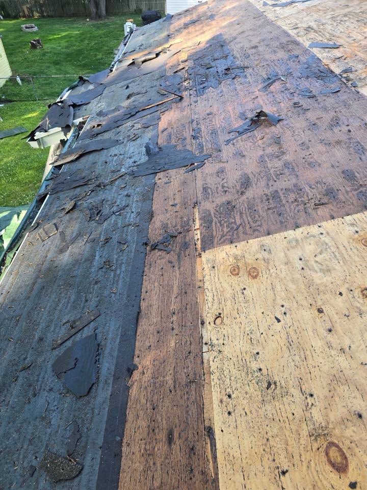Roof with torn black underlayment and exposed plywood decking, showing storm damage.