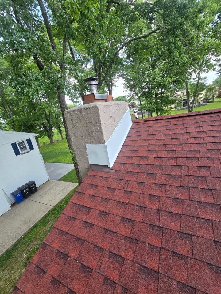 Red shingle rooftop beside a brick chimney, with green trees and a neighboring house visible.