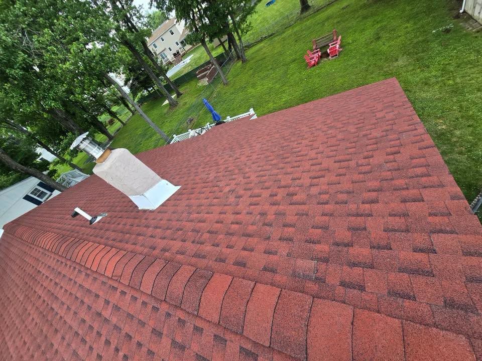Red shingled roof with vents, viewed from above, with green yard and red chairs in the background