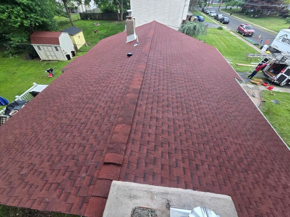 Roof seen from above, with red shingles, chimney, and neighboring homes and cars nearby.
