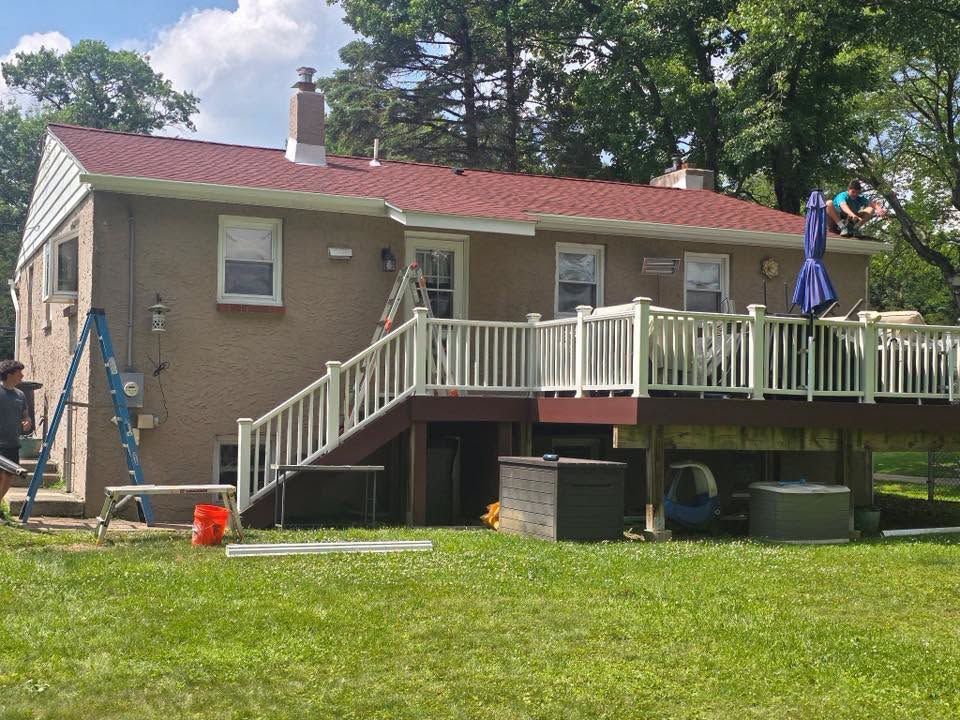 Single-story house with red roof and raised deck in a grassy yard, with a ladder and blue umbrella outside.