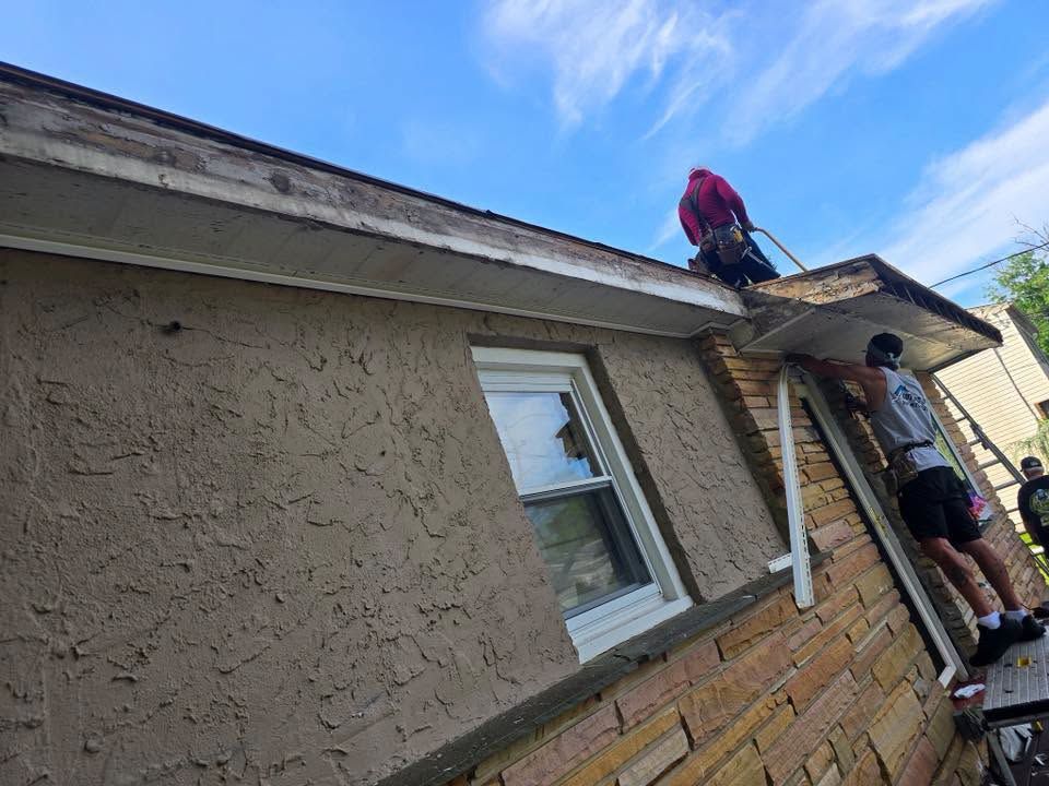 Two workers on a ladder repairing a shingled roof beside a stucco house