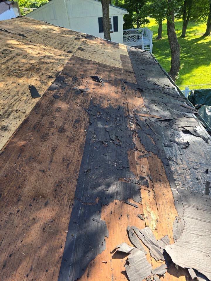 Partially stripped roof with old shingles and patches of exposed wood, viewed from above