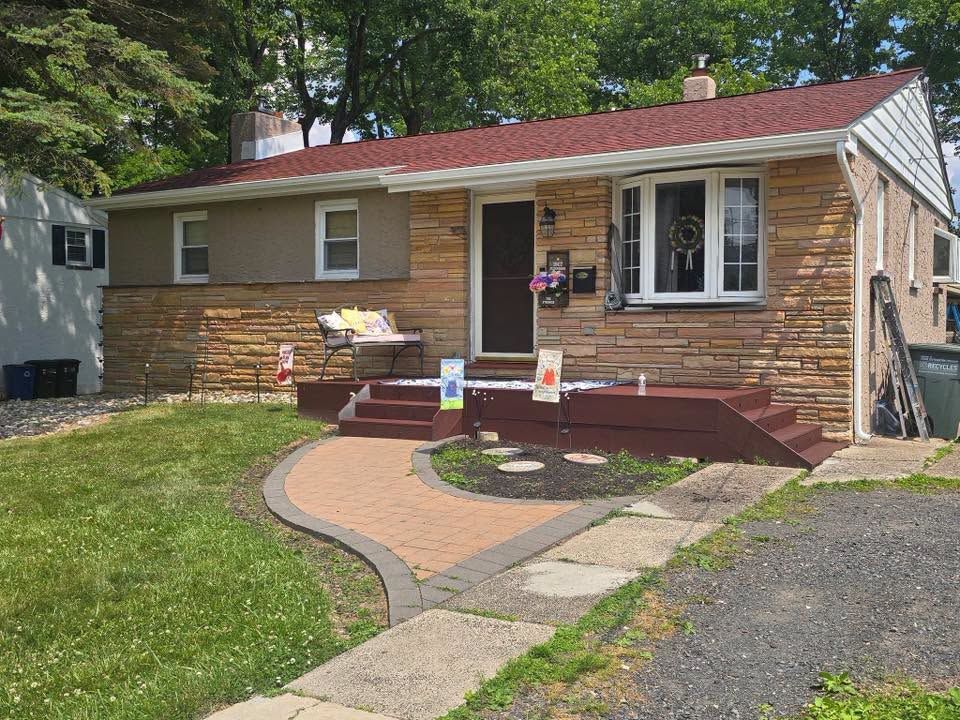 Single-story tan house with red roof, front porch, curved walkway, and a parked car in the yard