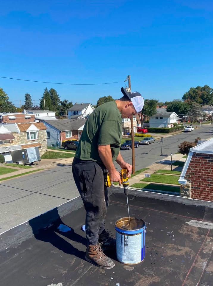 Worker on a rooftop mixing material in a blue bucket on a sunny day.