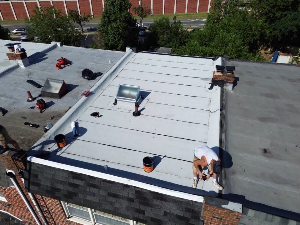 Rooftop with white membrane and vents, surrounded by gray roof sections and a brick wall backdrop