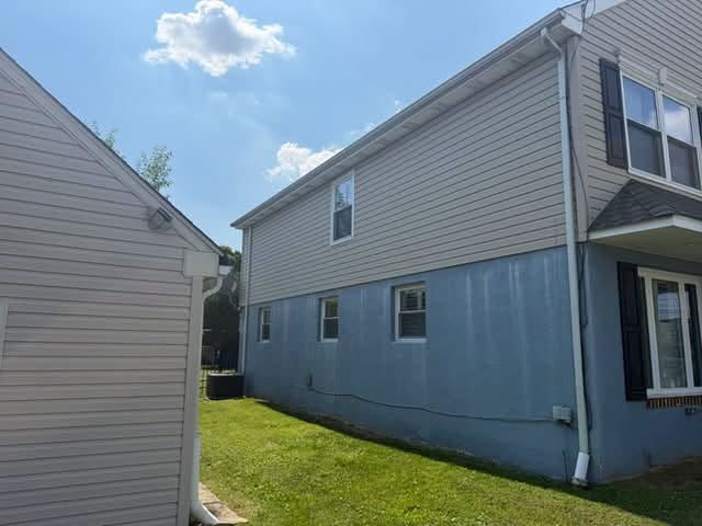 Narrow grassy space between two beige-sided houses under a blue sky with clouds