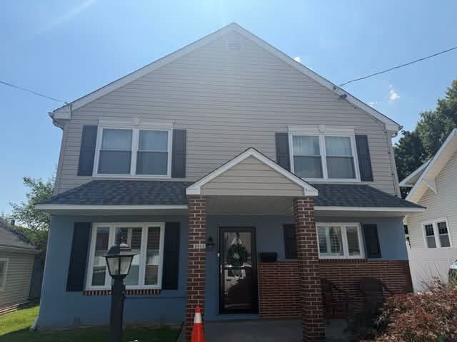 Two-story house with gray siding, red brick accents, and a small covered front porch
