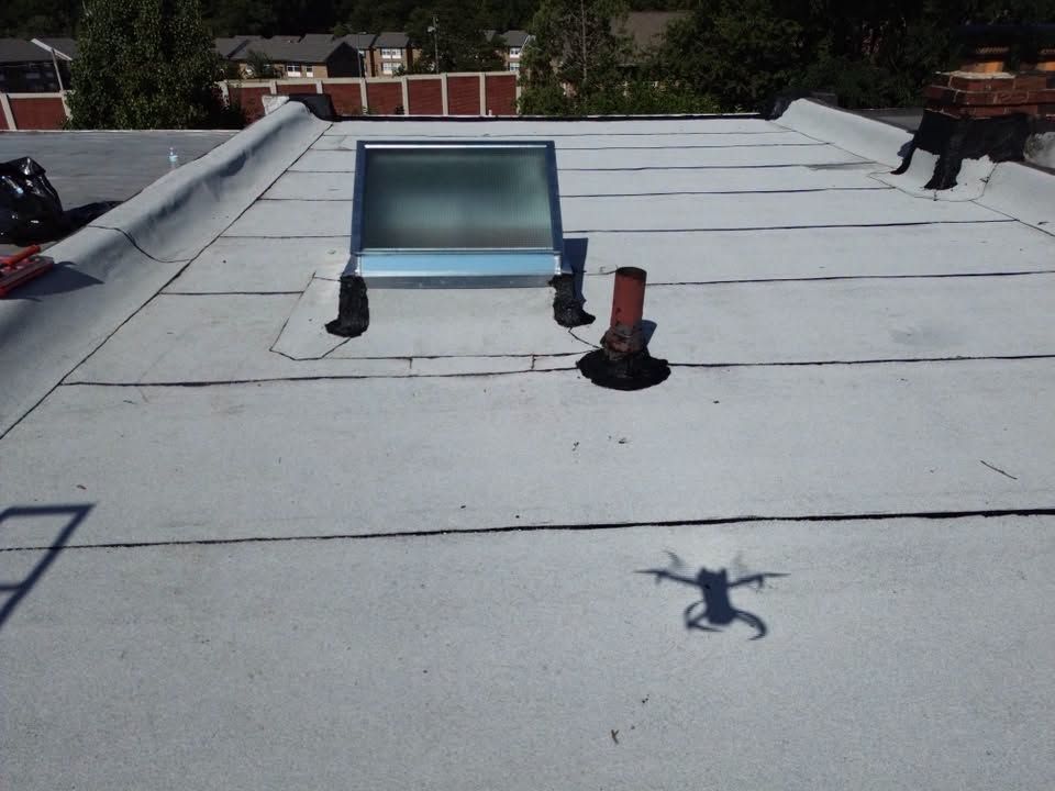 Rooftop with a skylight, vent pipes, and a small drone shadow on the white roof surface.