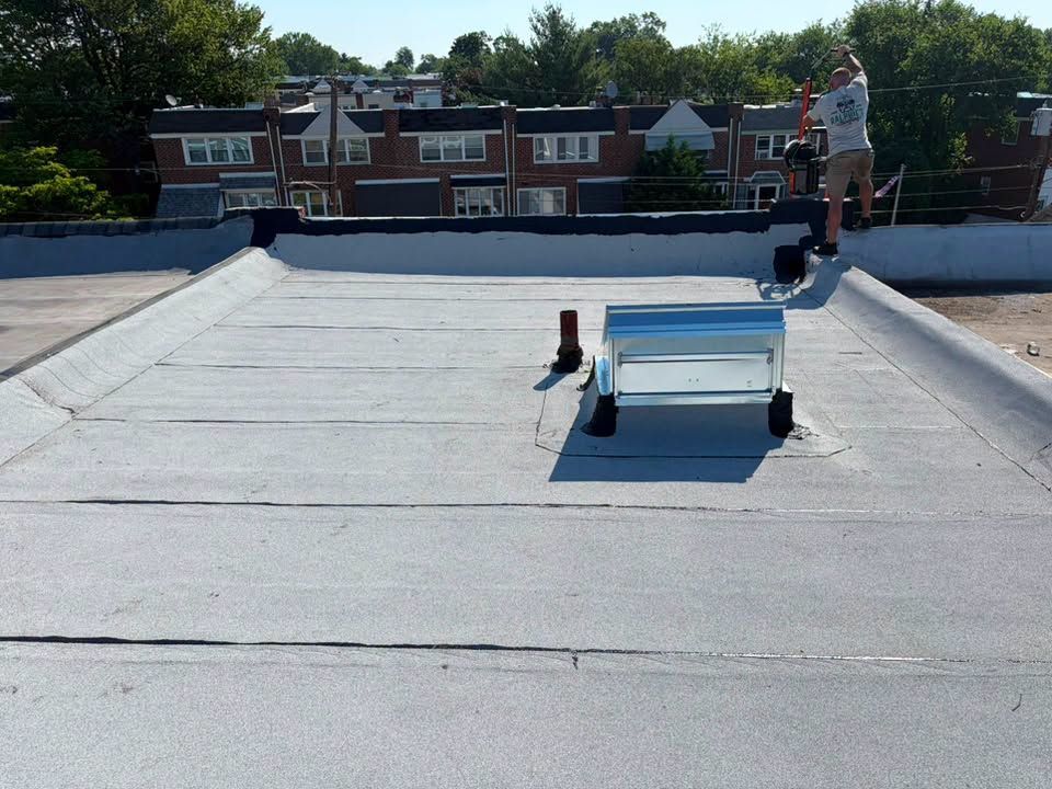 Roofer on a flat white roof near a skylight, with brick townhouses and trees in the background
