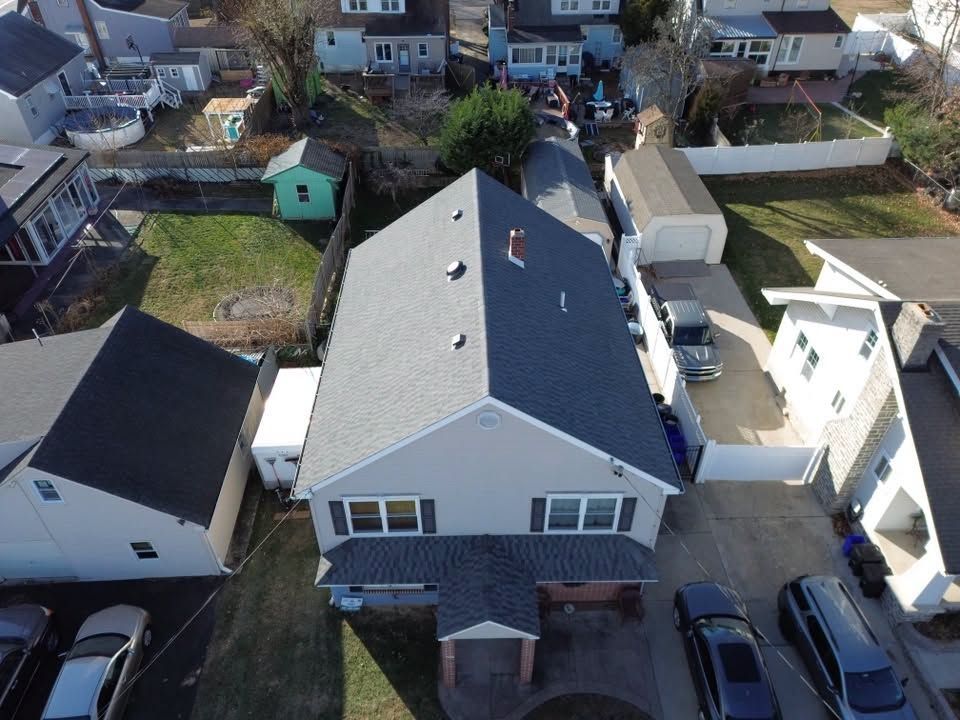 Aerial view of a gray-roofed house with neighboring homes and parked cars in a residential neighborhood