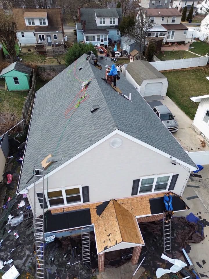 Workers on a house roof during repairs, with ladders and building materials in a residential neighborhood.