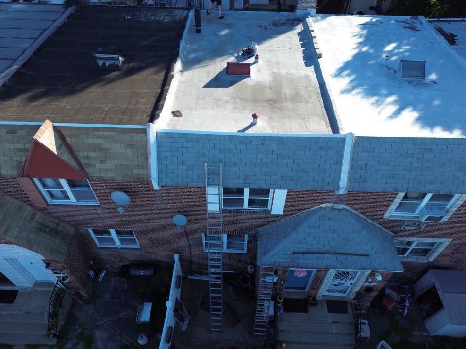 Aerial view of a brick townhouse roof with snow and rooftop vents, showing a rear exterior staircase and patios.