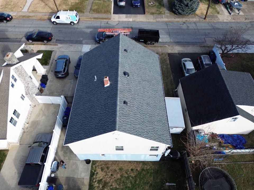 Aerial view of a white house with a gray roof beside a street and parked cars.
