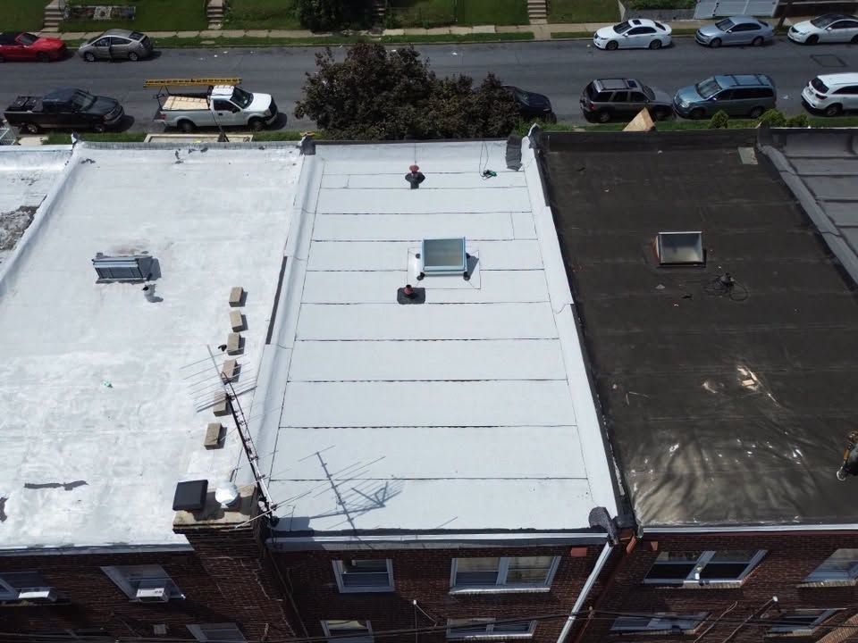 Aerial view of three flat rooftops beside a street with parked cars and trees