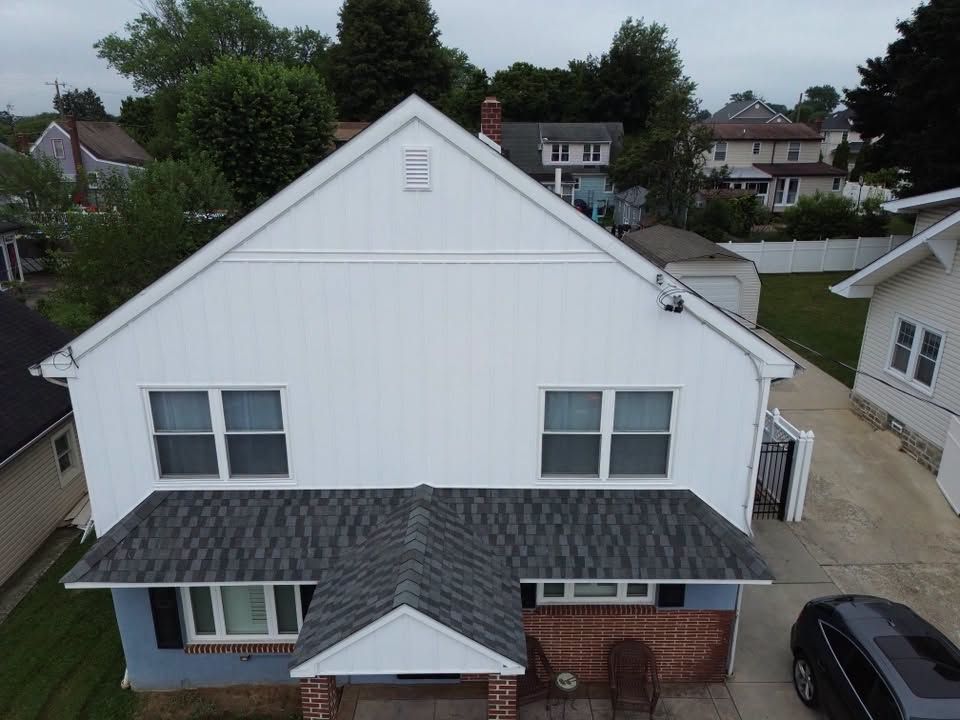 Aerial view of a white two-story house with a dark roof and a small front porch in a suburban neighborhood