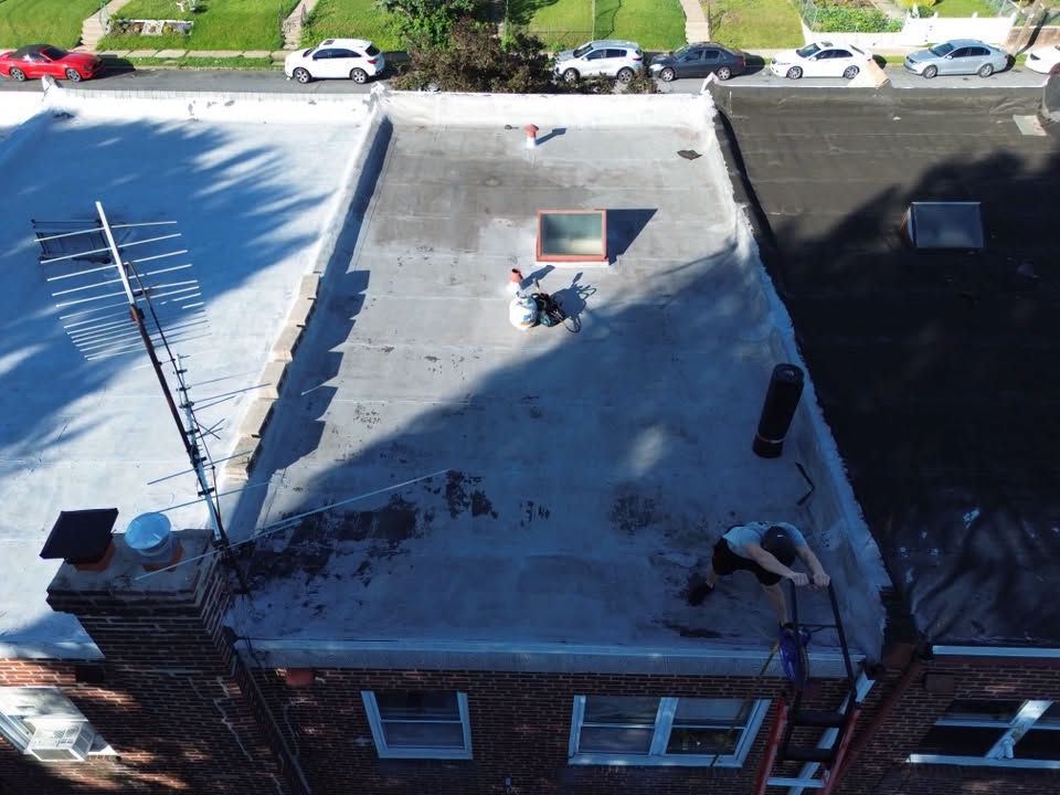 Aerial view of a flat roof with snow patches, rooftop vents, and a person working near the center.