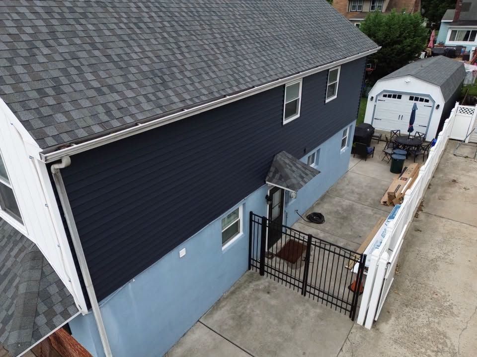 Aerial view of a blue house with a fenced side yard, driveway, and detached garage behind it.