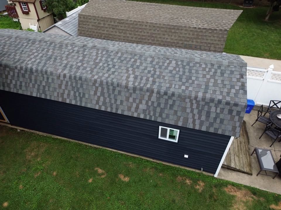 Aerial view of a dark blue house with a gray shingle roof and a small patio beside it