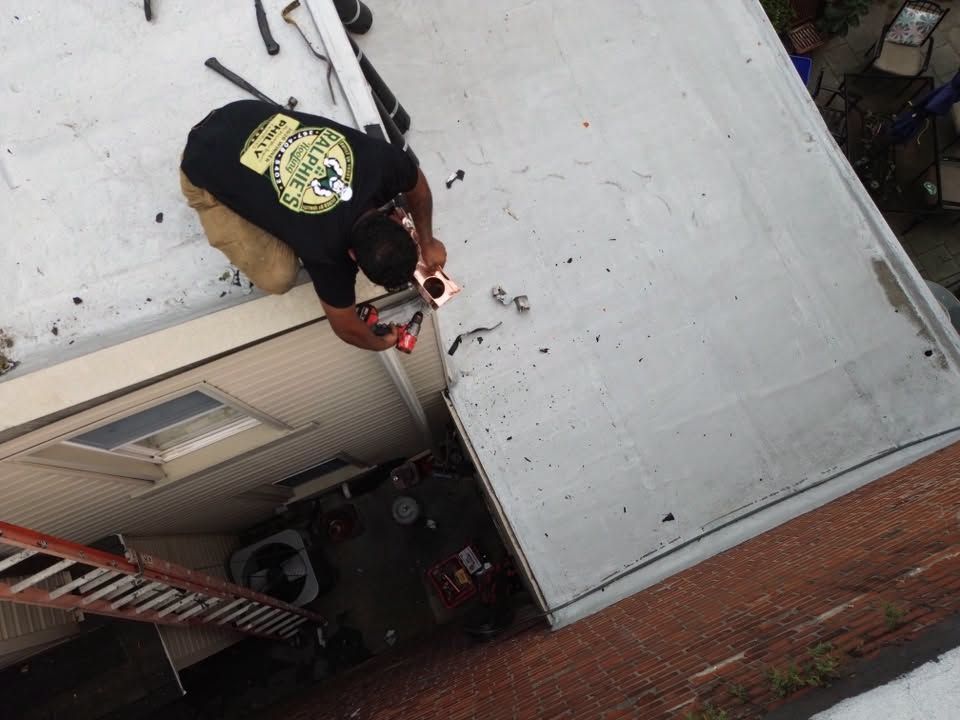Person on a roof using red power tools beside a ladder and brick wall below