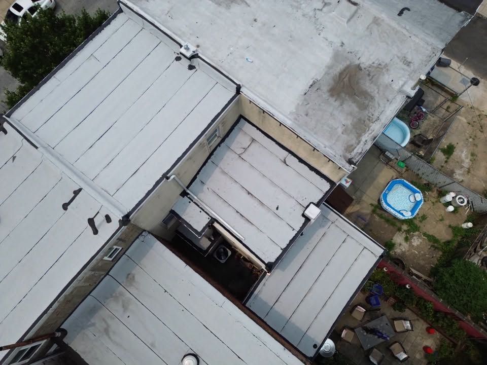 Aerial view of white rooftops around a narrow courtyard with scattered items and a blue kiddie pool.