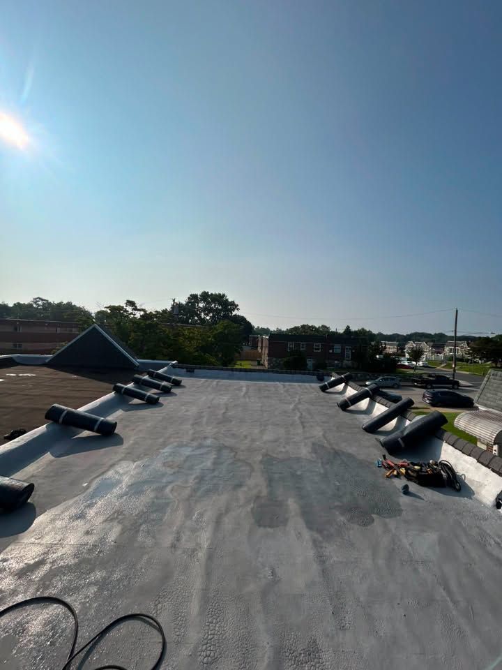 Flat rooftop with gray surface, vents and equipment, under a clear blue sky.