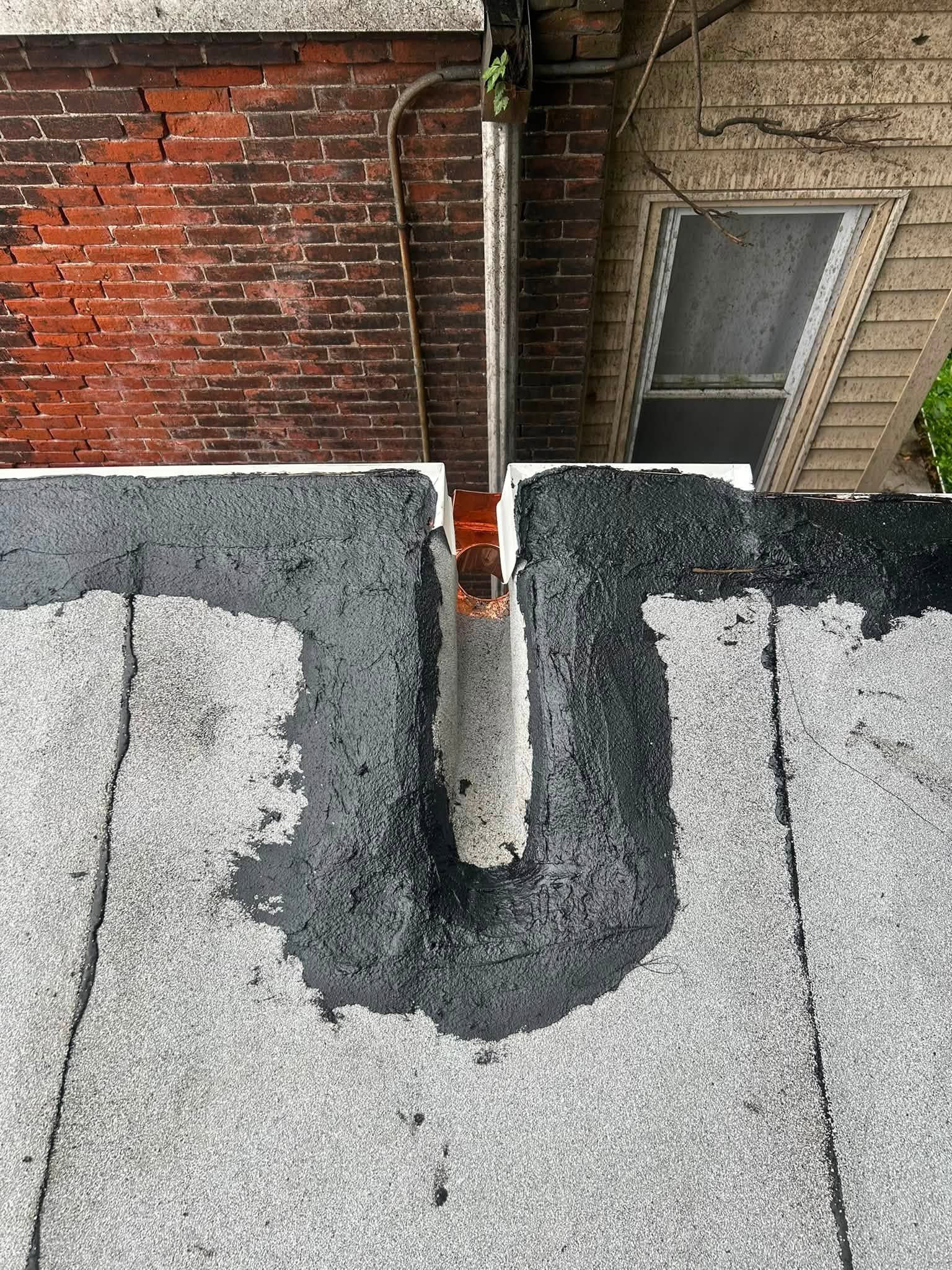 Rooftop with a metal pipe vent between a red brick wall and a beige building wall.