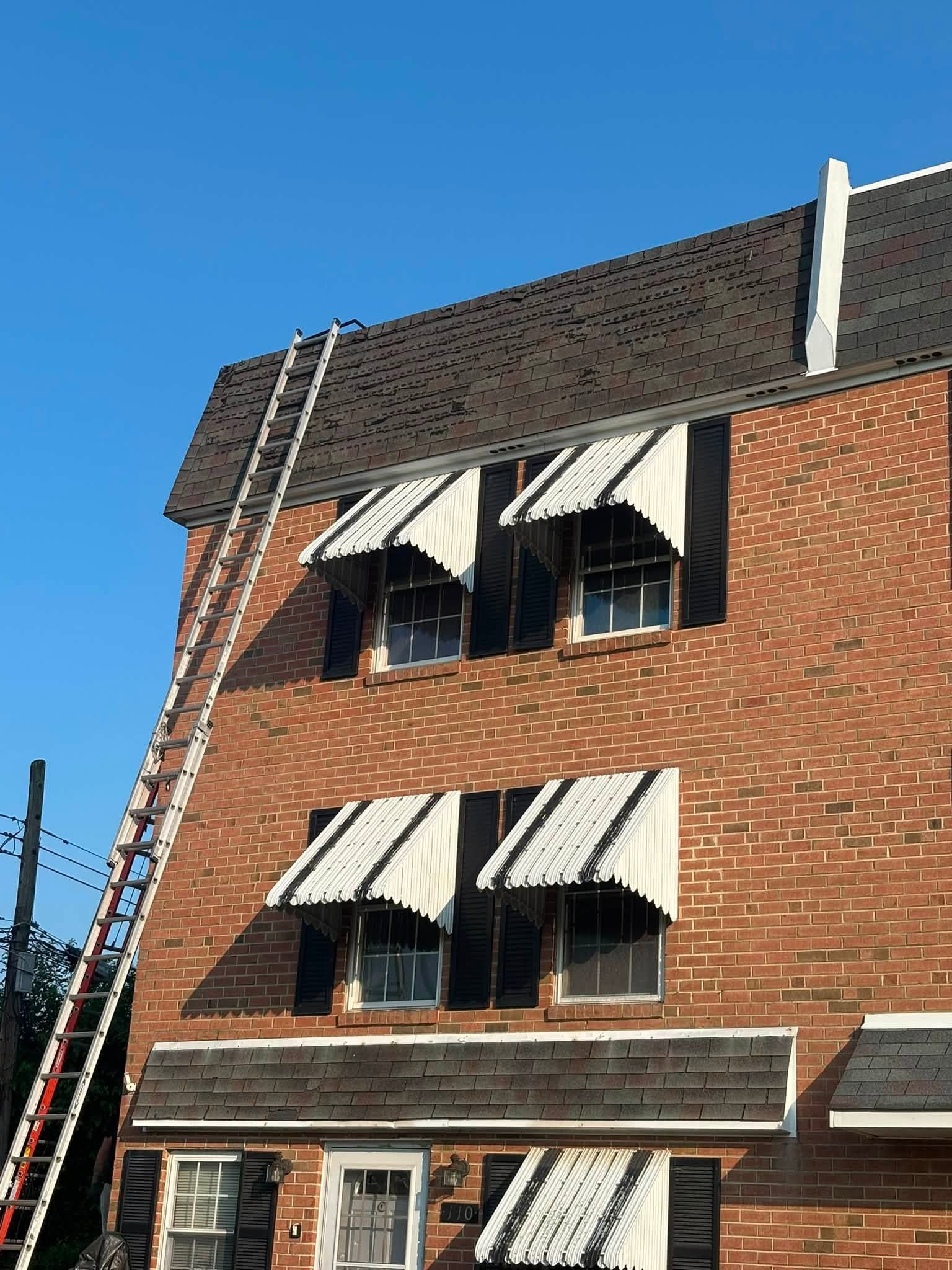 Brick building with striped awnings and a long red ladder leaning against the roof under a blue sky