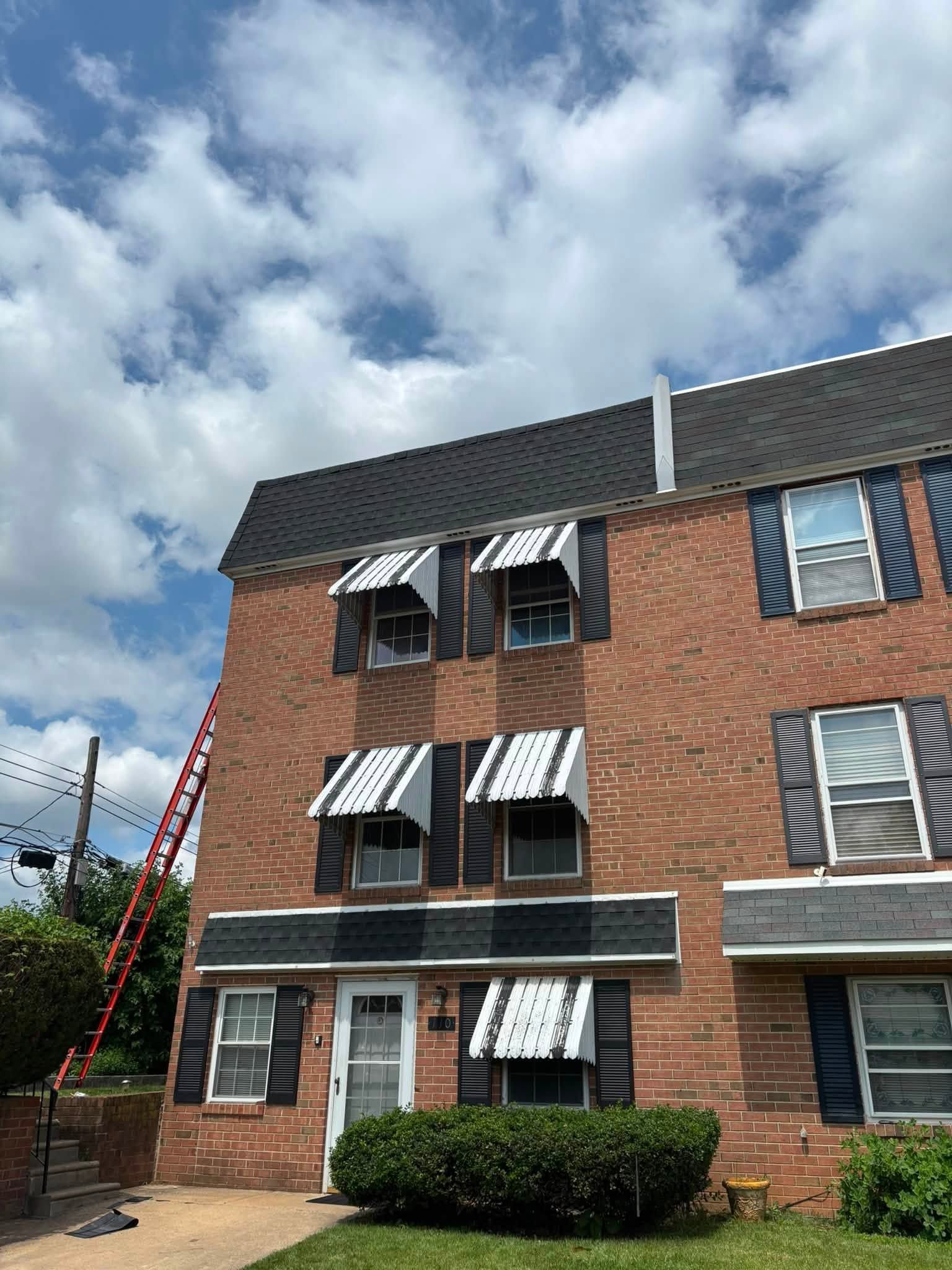 Brick apartment building with dark awnings and a red ladder against the side under a cloudy sky