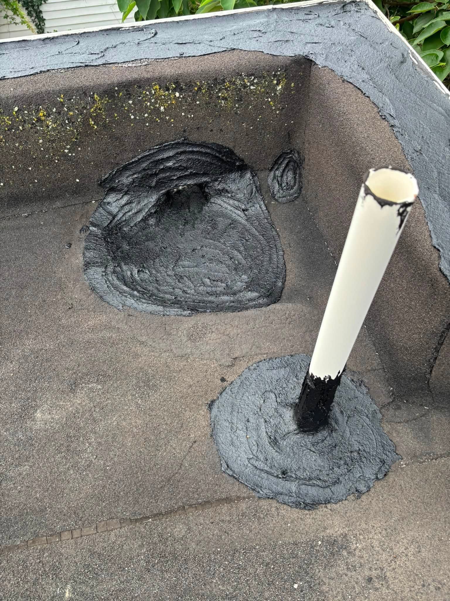 Flat rooftop with a large dark patch and a white pipe emerging from a sealed base.