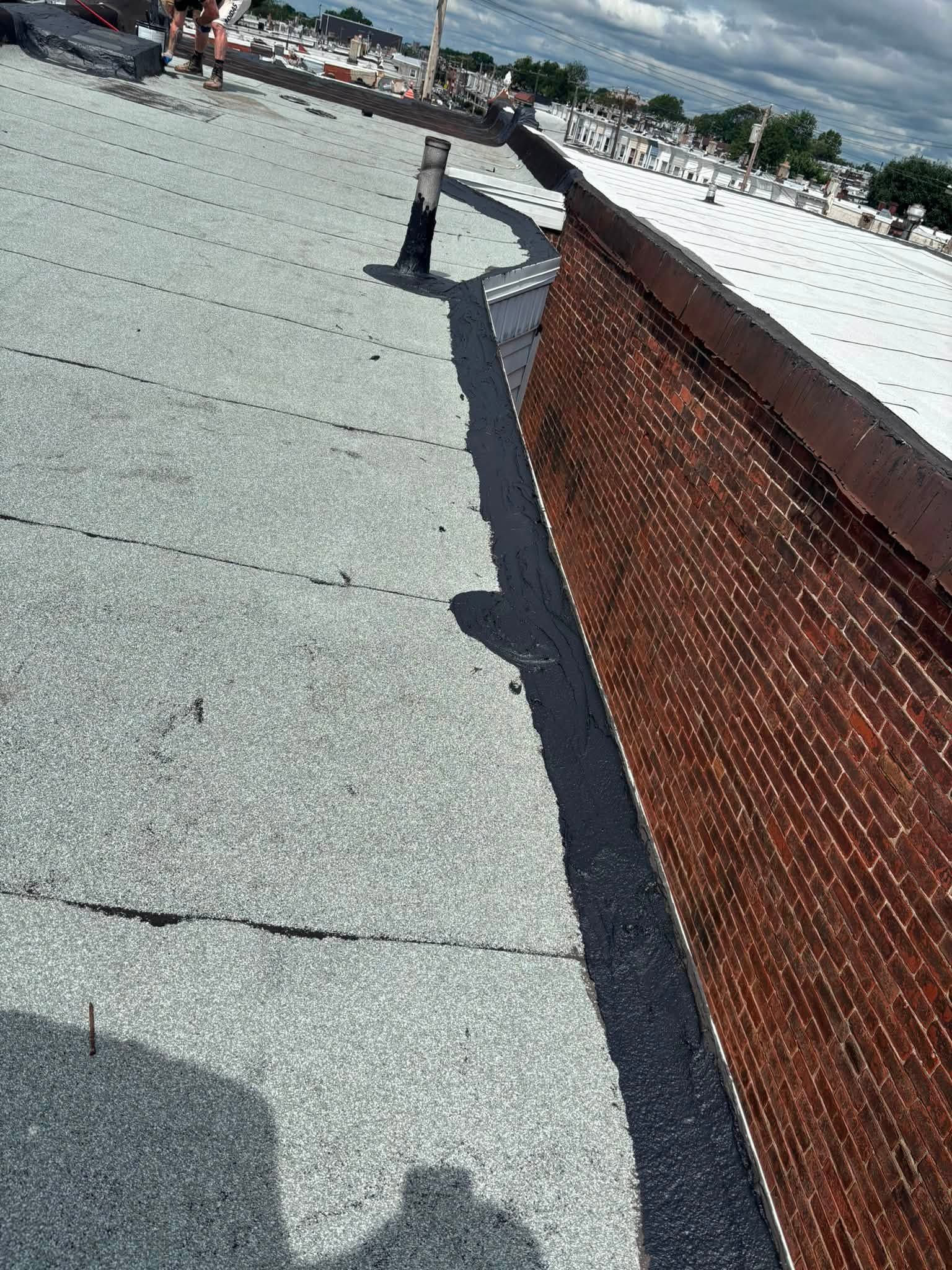 Rooftop with gravel surface and brick parapet wall beside a snowy, tree-lined edge