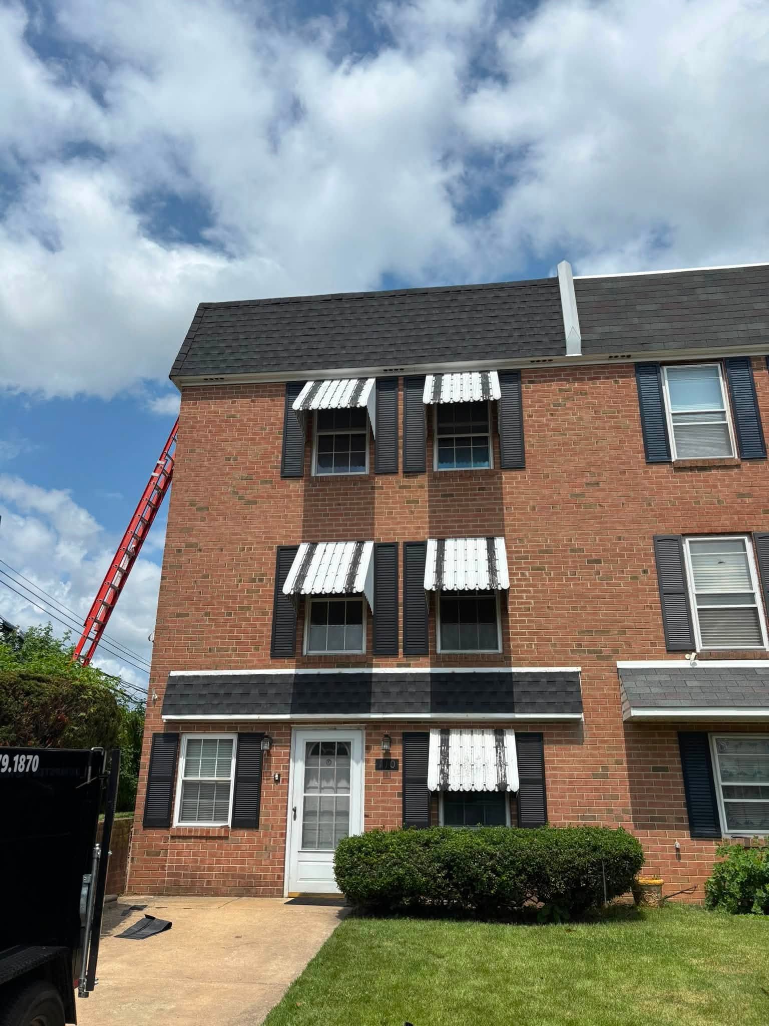Three-story brick townhouse with striped awnings and a red ladder under a partly cloudy sky