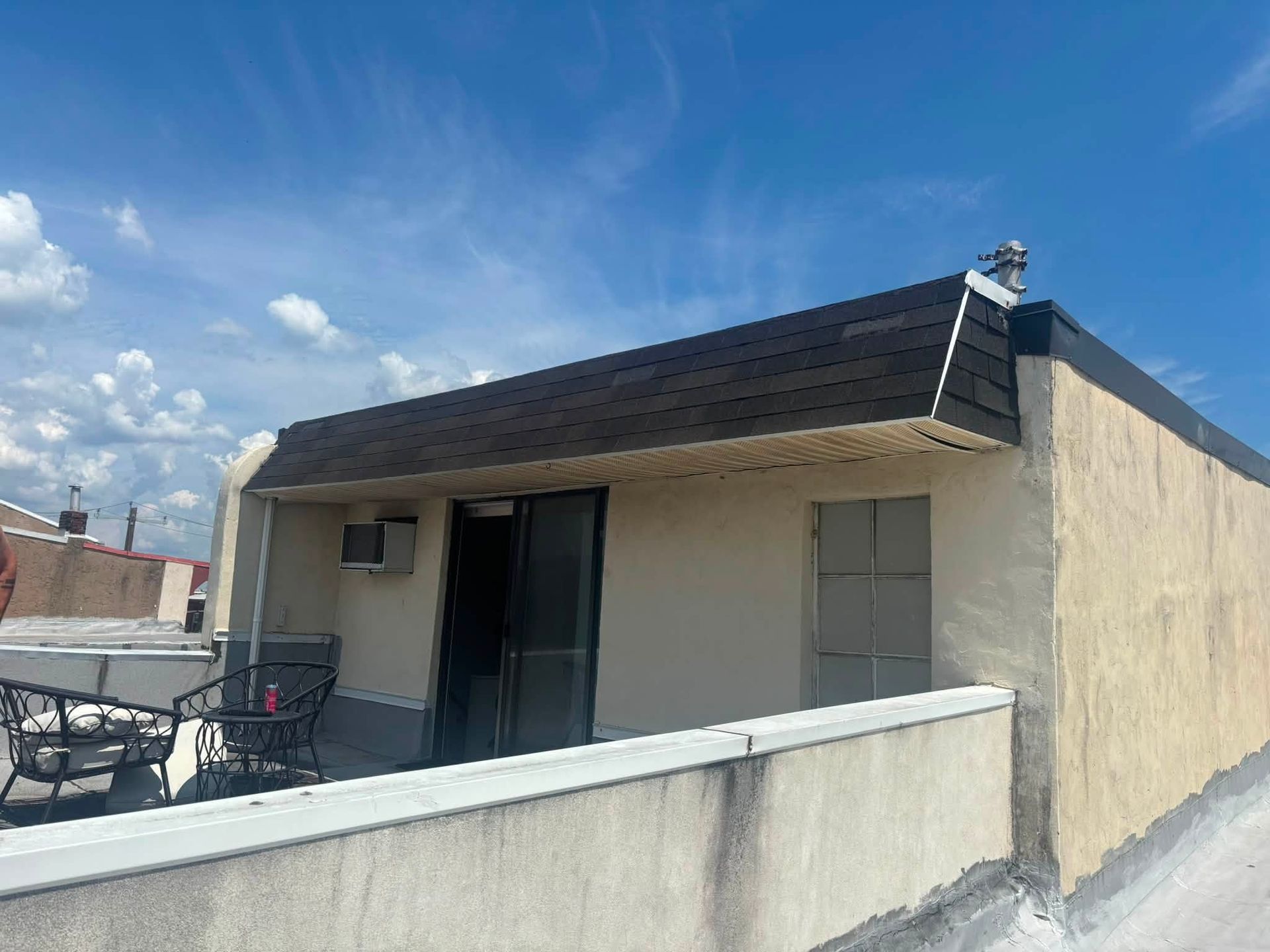 Small beige house with a dark roof and low white wall under a blue sky.