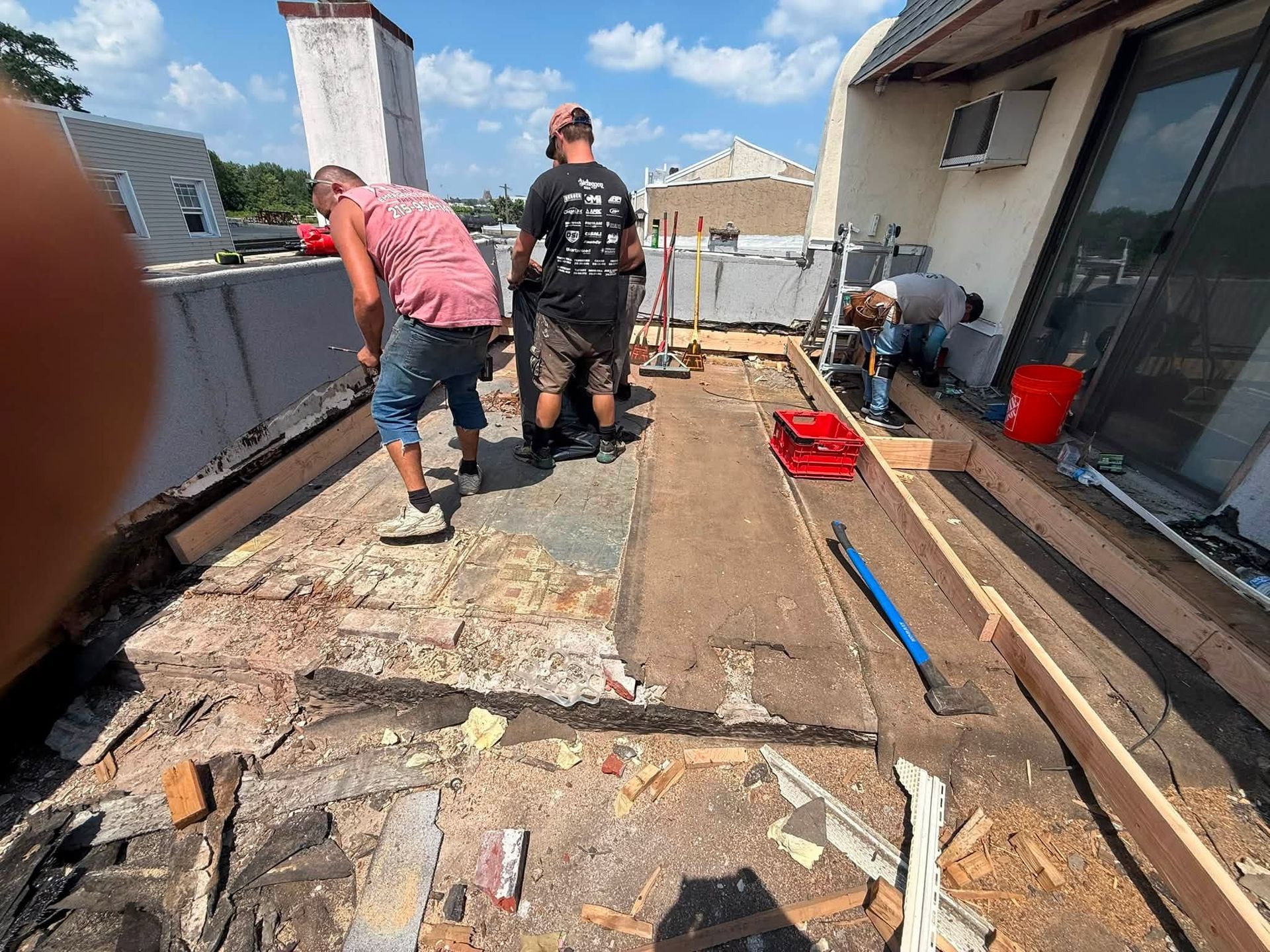 Workers repairing a rooftop deck with tools, wood planks, and debris under bright sunlight