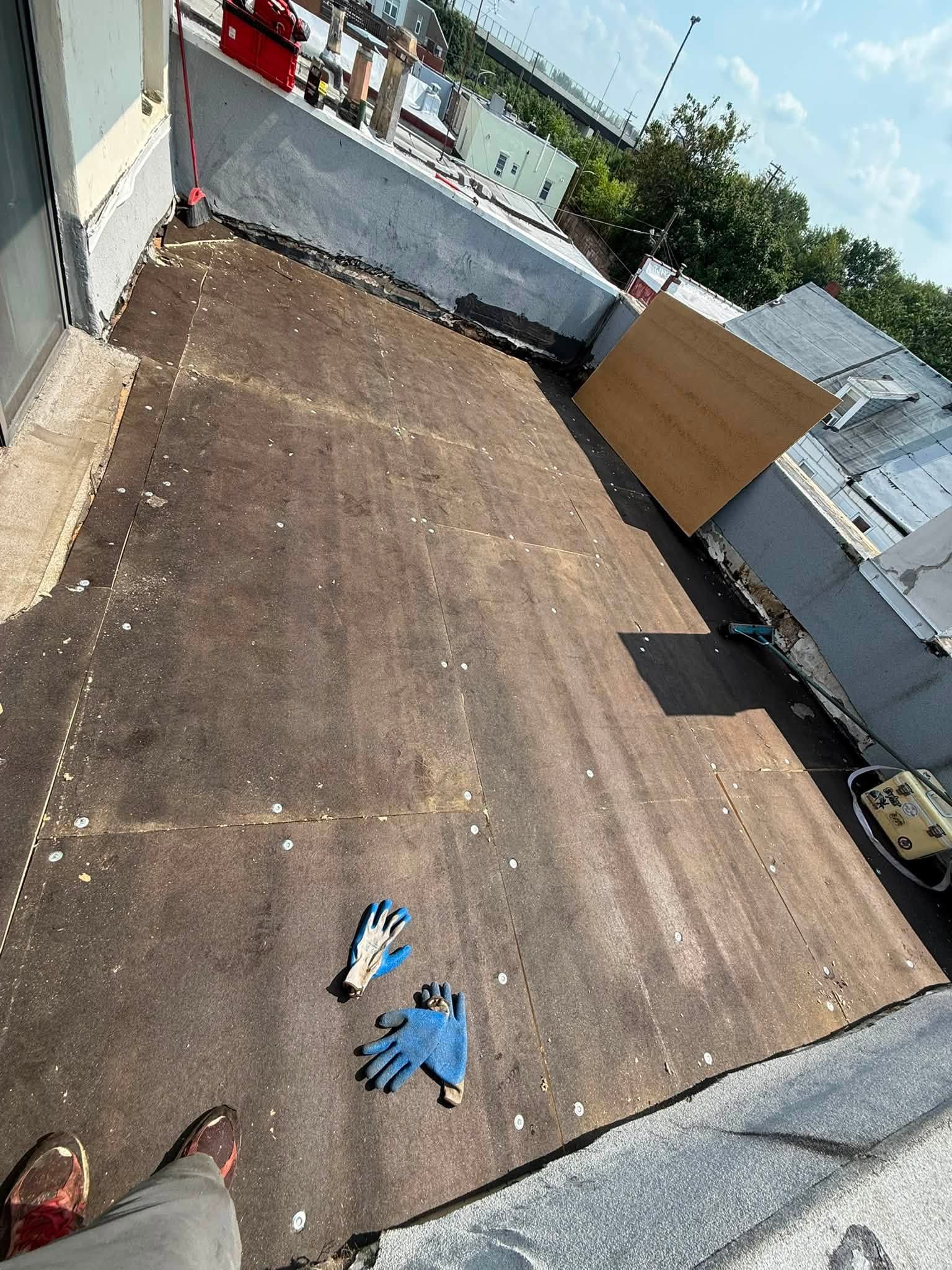 Empty rooftop terrace with brown flooring, gray walls, a cardboard panel, and a few shoes near the foreground.