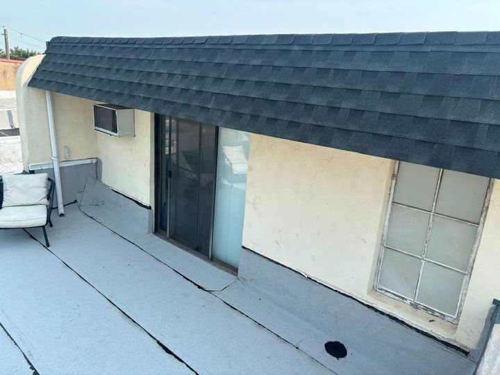 Rooftop with dark shingles, sliding glass door, small windows, and patio furniture along a cream wall