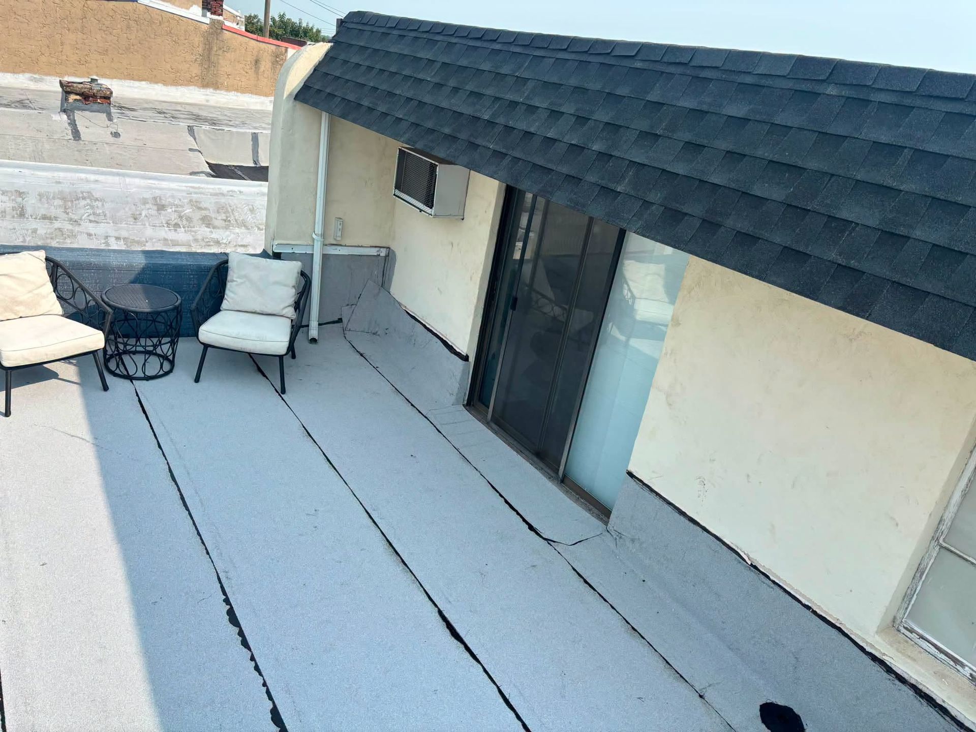 Rooftop patio with gray flooring, black patio furniture, and sliding glass doors beside a white building