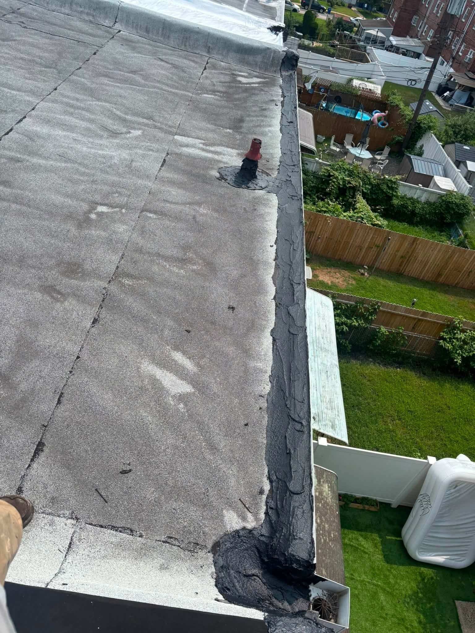 Rooftop with gray concrete surface, a person near the edge, and houses and greenery below.
