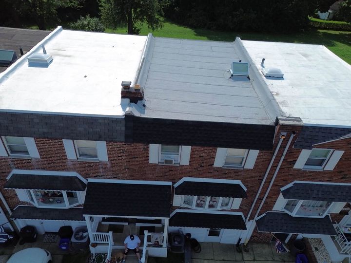 Aerial view of a row of brick townhouses with flat white roofs and small front porches.