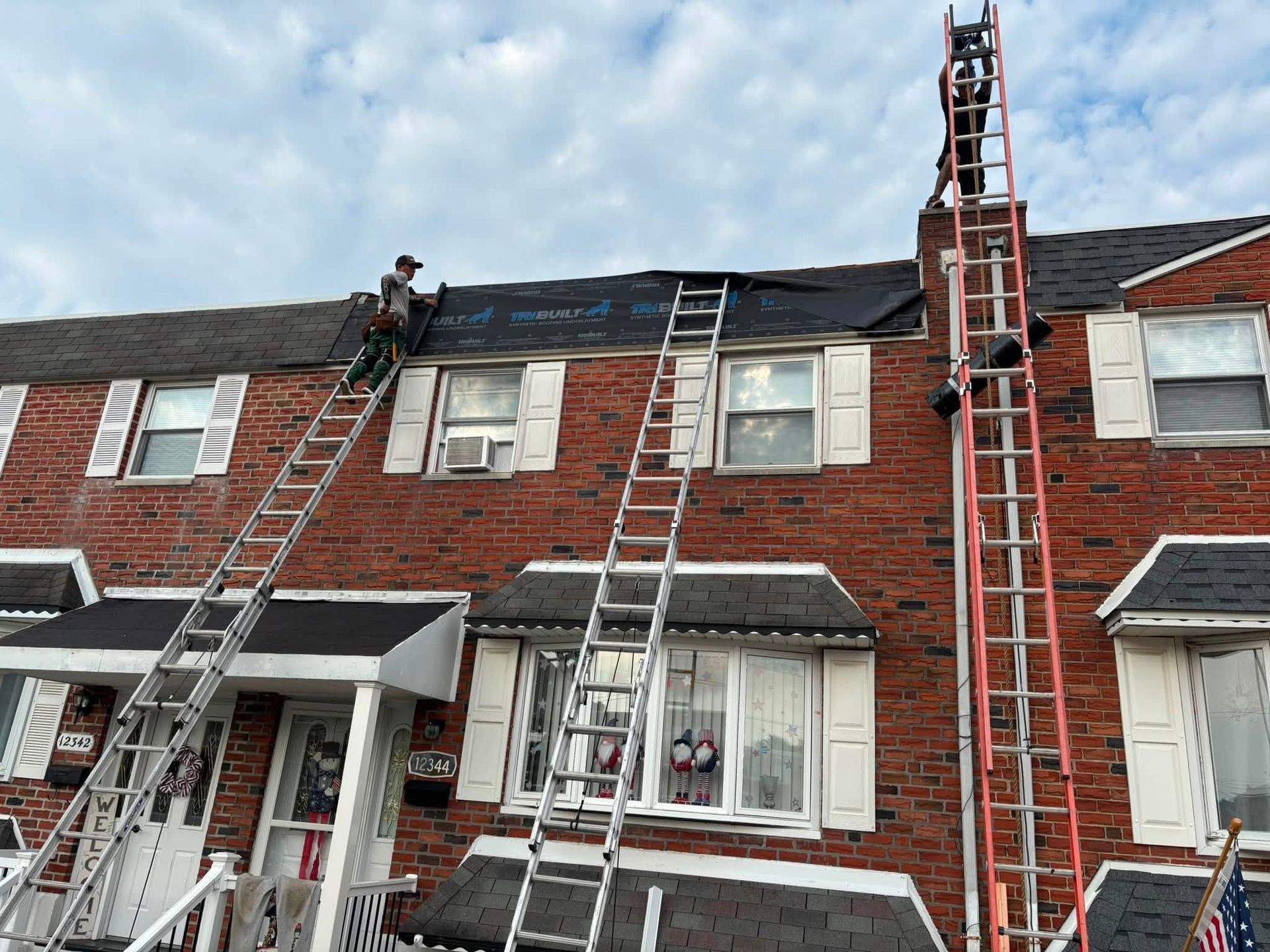 Ladders leaning against brick row houses with roofers working on the roofs
