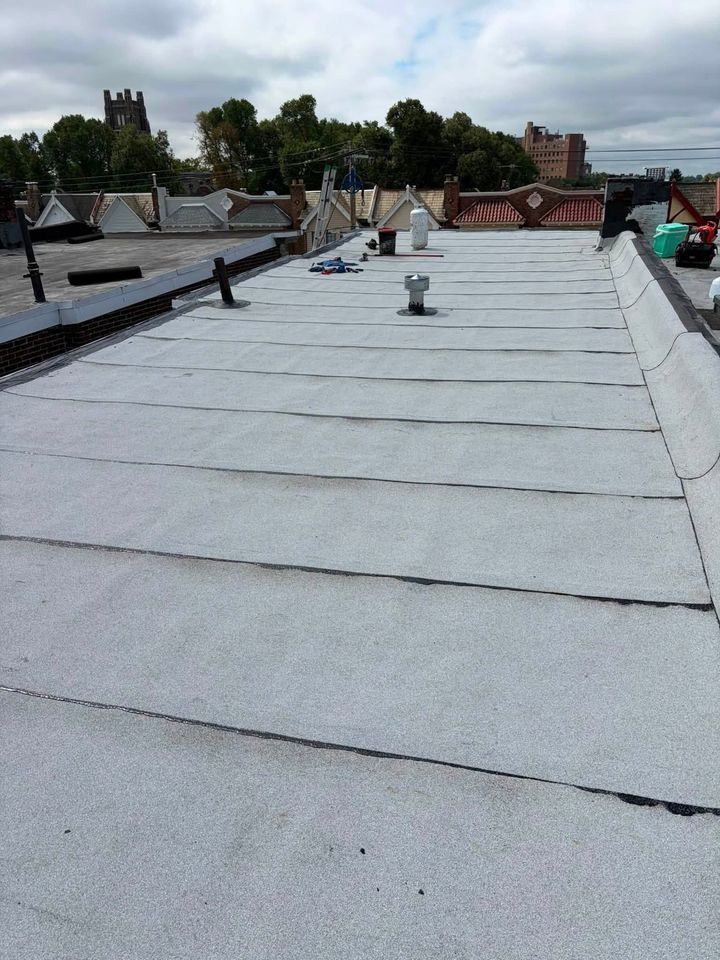 Flat gray roof under construction with workers and rooftop vents in the distance