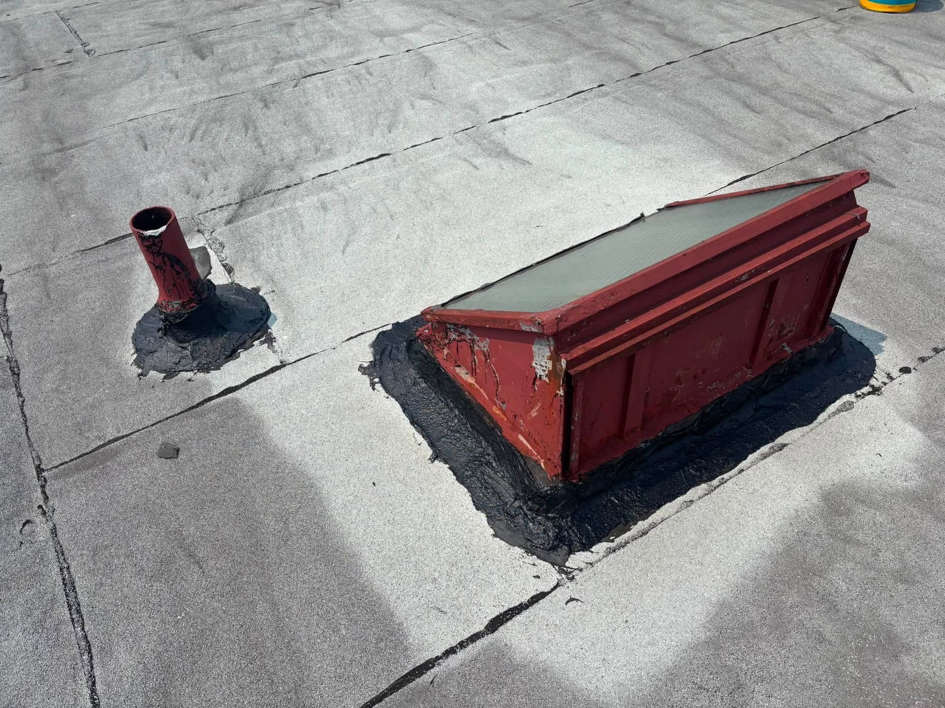 Red rooftop vent and pipe on a gray flat roof with sealing patches nearby