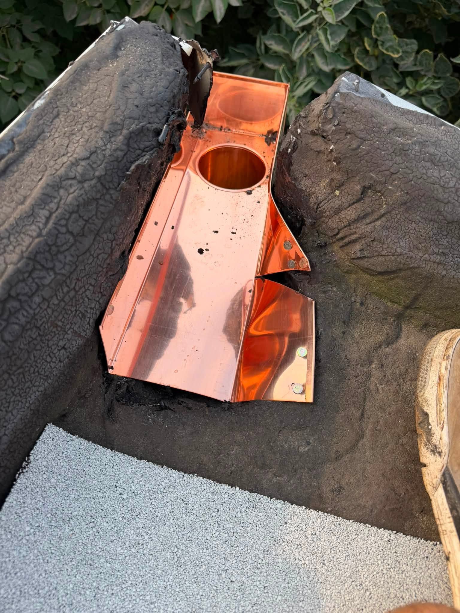 Damaged copper roof flashing around a vent pipe, with torn tar paper and debris