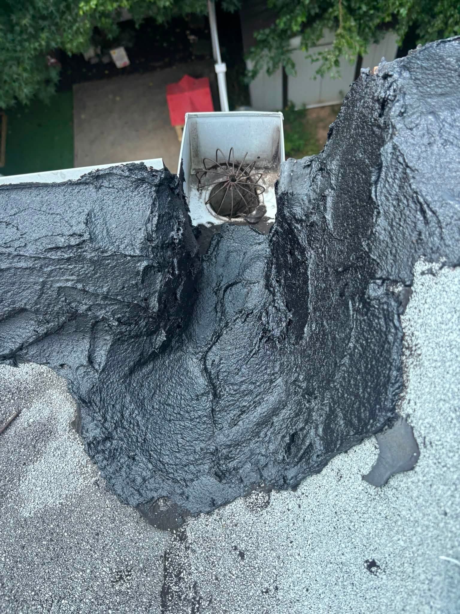 Roof with damaged black coating around a metal vent pipe and debris near the opening