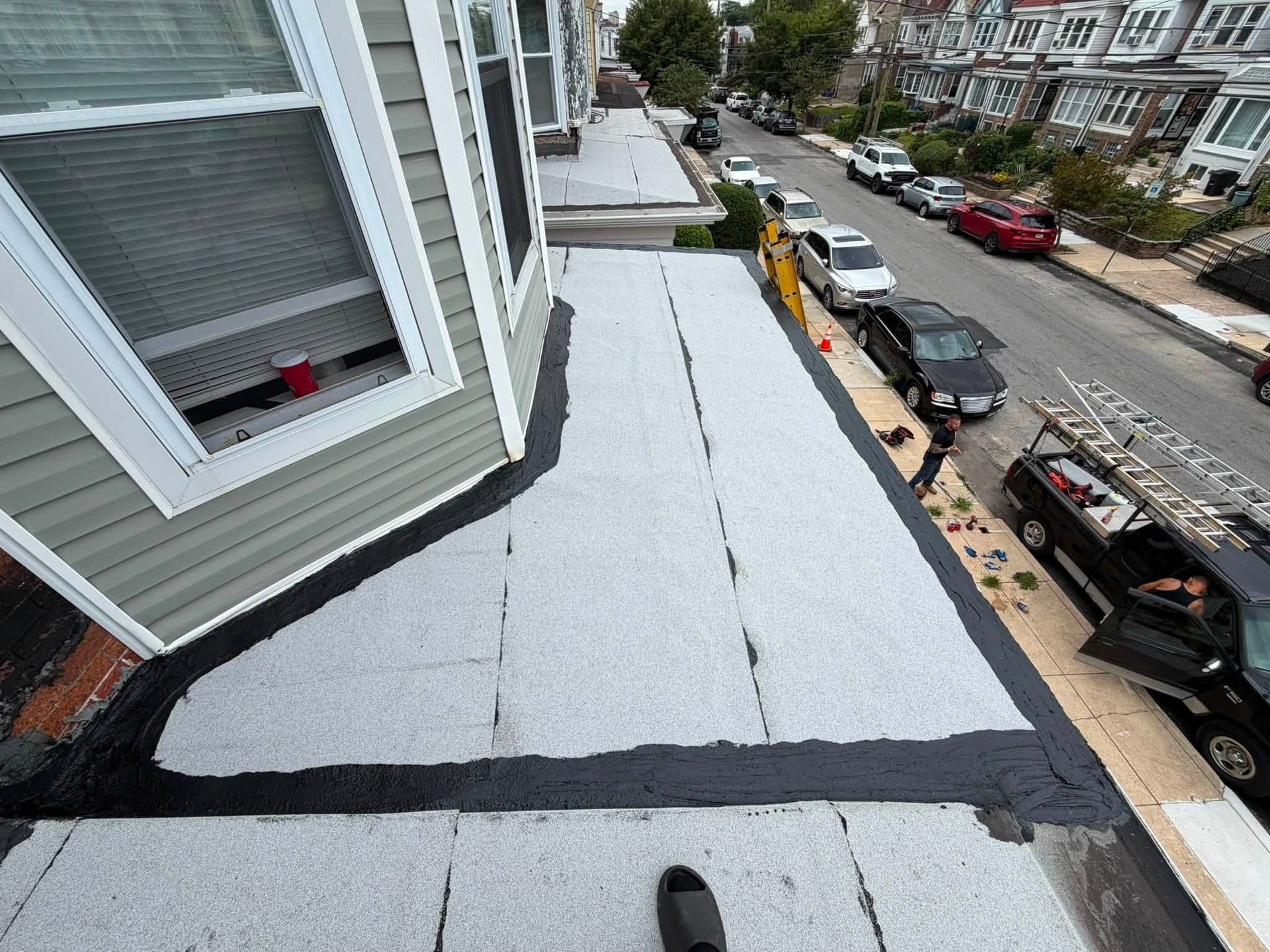 Roof with fresh white coating beside a row of parked cars on a city street.