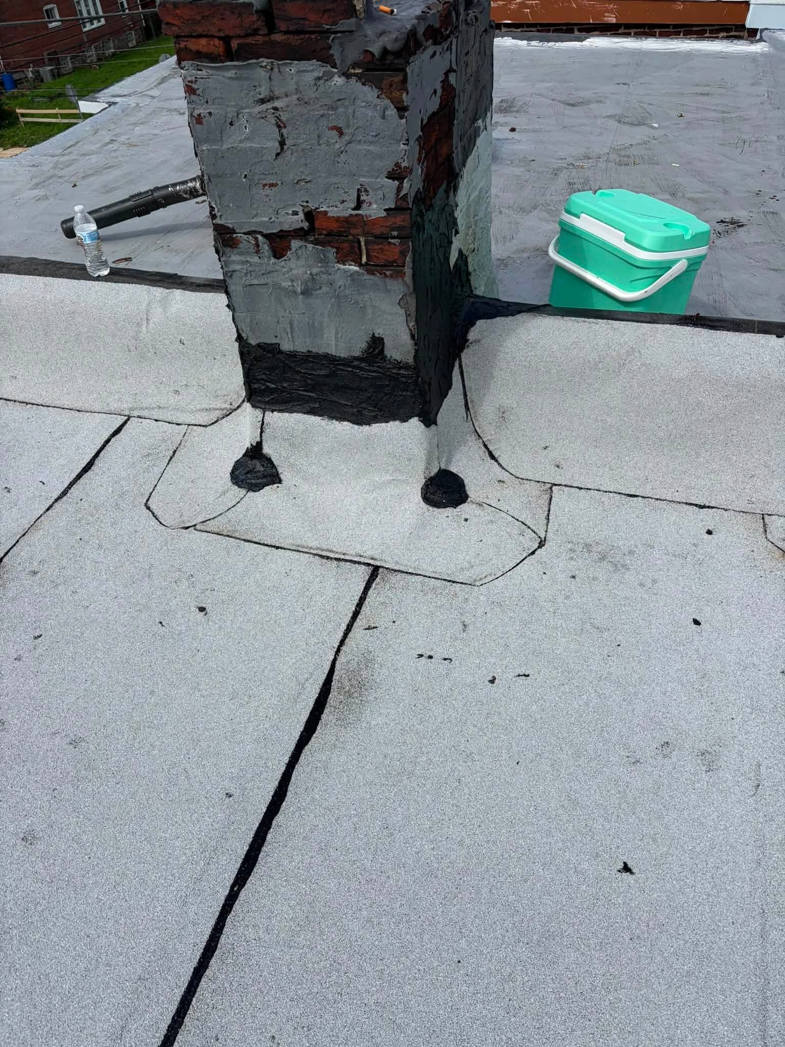 Rooftop vent base with weathered metal and a green container on a flat gray roof.