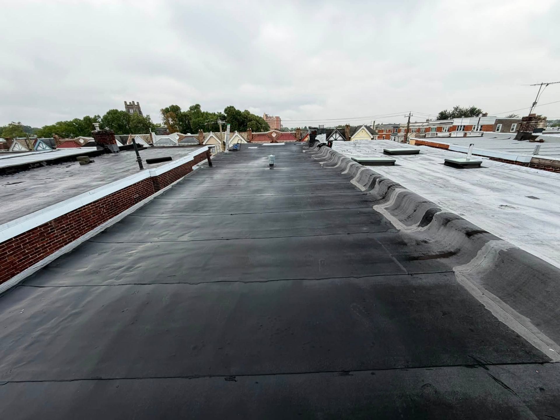 Flat rooftop with black waterproof membrane and low parapet walls under an overcast sky