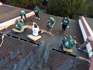 Workers repairing a shingled roof, with tools and materials spread across the top.