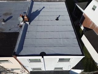 Aerial view of a flat gray rooftop with two workers near a ladder and a shadow cast across the roof.