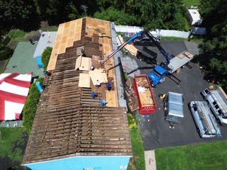 Aerial view of roof repairs with a crane and workers beside a large building and construction materials